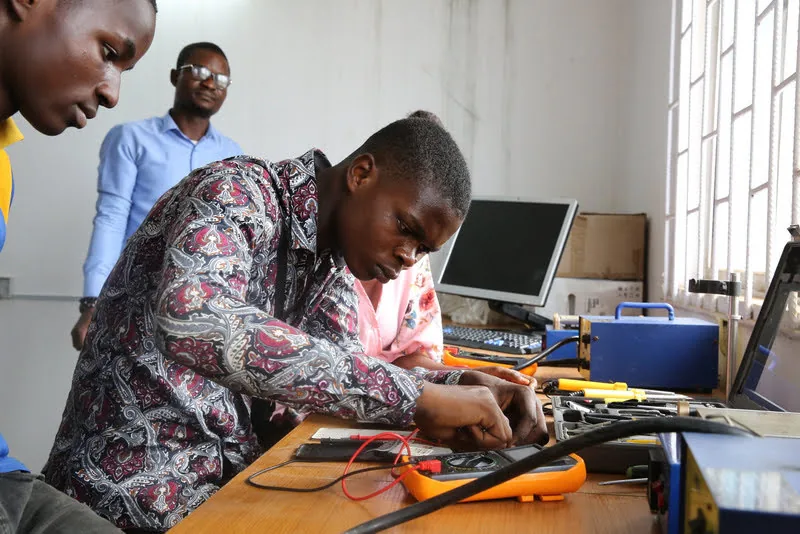 Learners and an instructor investigating electronic equipment at a workbench